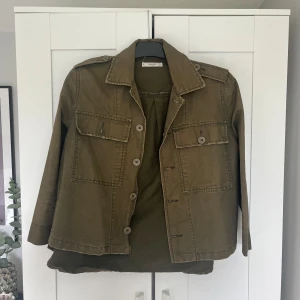Olivgrön jeansjacka  - Säljer en olivgrön jeansjacka från Mango med klassisk krage, axelklaffar och stora bröstfickor med knappar. Jackan är i bomull och har en avslappnad passform, perfekt att slänga över en hoodie eller t-shirt. Stängs med knappar framtill. Använd få gånger. Pris går att diskutera!