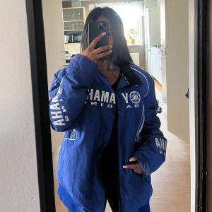 Blå Yamaha Racing  - Säljer en skit cool blå Yamaha Racing vindjacka med stora Oversized passform och tillverkad i slitstark polyester – perfekt för dig som gillar sportig stil.  OBS två skavanker. En fram och en bak. Det är färg tror jag.