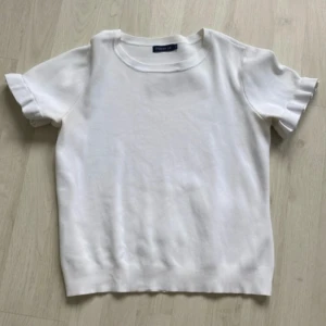 Vit stickad tröja från Stockh LM - Supersöt vit stickad tröja från Stockh LM i storlek XS. Tröjan har korta ärmar med volangdetalj och rund halsringning. Perfekt till vår och sommar för en clean och fräsch look. Materialet är mjukt och stretchigt för extra komfort.