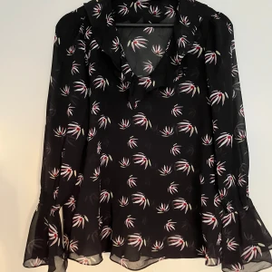 Svart mönstrad mesh blus - Supersnygg svart genomskinlig blus med ärmar som är lite flowy i slutet av ärmen. V-urringning med volanger. 