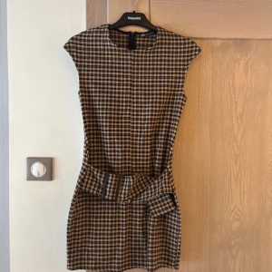 Rutig kortklänning med bälte från Zara  - Supersnygg rutig kortklänning från Zara i beige och svart. Klänningen har en figurnära passform, är ärmlös och kommer med ett matchande bälte i midjan. 