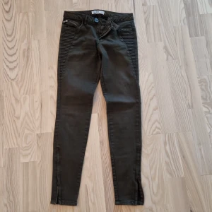Mörkgröna lågmidja skinny jeans Zara Basic - Snygga mörkgröna skinny jeans från Zara Basic med coola ribbade detaljer på sidorna, dragkedjor vid bensluten och en liten ficka med dragkedja fram. Jeansen är i stretchigt denim och har en modern look som passar till allt.