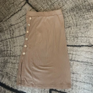 Beige ribbad kjol med knappar - Säljer en beige ribbad kjol med snygga knappar längs sidan och en liten slits nedtill. Kjolen är midilång och har en tight passform som framhäver siluetten. Perfekt för dig som gillar stilrena och enkla plagg med en twist. Från Vera Moda. Strl s. Går att diskutera pris 