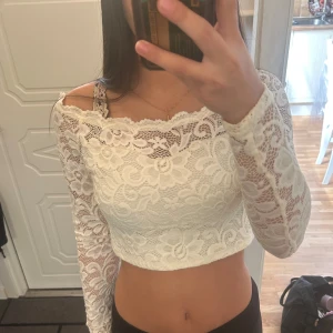 Vit croppad spetsblus med lång ärm - Säljer en superfin vit croppad blus i spets. Toppen har långa ärmar och en offshoulder-skärning som ger en snygg och trendig look. 