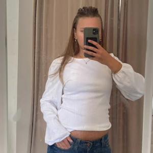 Vit långärmad topp från Vero Moda - Vit långärmad topp från Vero Moda med lätt puffade ärmar och strukturerat tyg. Enkel och stilren modell med rund halsringning, perfekt till jeans eller kjol. Materialet känns mjukt och har en lätt stretch för skön passform. Den har också gula fläckar på framsida 