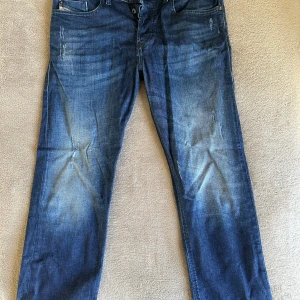 Diesel Jeans Slim Fit - Säljer ett par blå Diesel Buster jeans med slim-tapered passform. Jeansen har snygga slitningar och ljusare partier framtill och på bakfickorna. Klassisk femficksmodell med regular midja och coola detaljer. Perfekta för en avslappnad streetstil. | 30/32 | Priset är inte hugget i sten ❌