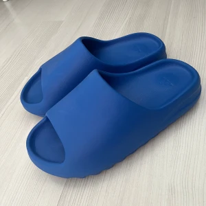 Yeezy slides azul - Säljer ett par Yeezy slides med färgen azul. Tofflorna har stilren design med bred rem över foten. Perfekta för sommaren eller att ha som inneskor. Skicket är bra med mindre repor. Storlek 10 us.
