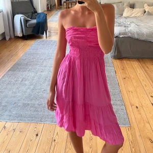 Rosa sommarklänning - Superfin tunn, ros, volangig klänning med smock upptill. Den går att bära axelbandslös eller knyta runt halsen. 