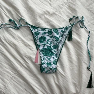 Grönblommig bikini från Design by Amor - Helt ny, oanvänd bikiniunderdel! Jättefint blommigt grönt mönster, och med knyt i sidorna. Perfekt för sommaren🩷