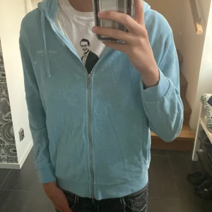 Ljusblå hoodie från Lexington - Ljusblå hoodie från Lexington i storlek S. Tröjan har huva med snörning, hel dragkedja framtill och ribbade muddar vid ärmslut och nederkant. Tillverkad i mjuk bomull, perfekt för chill dagar. Enkel och stilren design utan mönster.