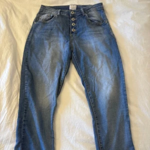 Blå jeans med knappar framtill - Snygga blå jeans med fem knappar framtill och klassiska fickor både fram och bak. Jeansen har en lätt tvättad look och raka ben. Perfekta för dig som gillar en avslappnad stil med lite edge.