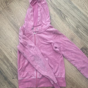 Rosa velour hoodie med dragkedja - Mjuk rosa hoodie i velour med huva och dragkedja framtill. Tröjan har långa ärmar, två fickor och ribbade muddar vid nederkant och ärmslut. Perfekt för chill dagar eller när du vill ha något comfy och snyggt på dig.