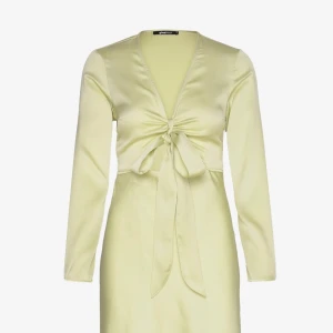 Ljusgul långklänning från Gina tricot  - Superfin ljusgul långklänning . Klänningen har lång ärm, v-ringning och snygg knytning framtill som ger en feminin touch. Perfekt för dig som vill sticka ut med en elegant och trendig look. (OANVÄND)