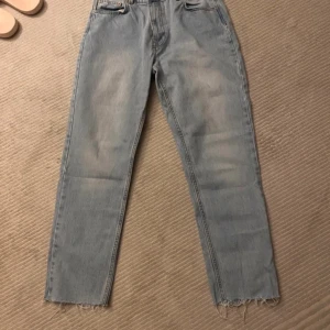 Ljusblå tapered jeans från NLY Jeans - Säljer ett par ljusblå jeans från NLY Jeans i modellen mid waist tapered leg. Jeansen har råa, fransiga benslut och klassisk femficksdesign. Tillverkade i 100% bomull för en skön och avslappnad känsla.