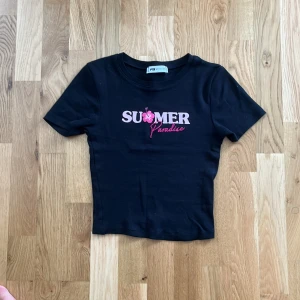 Svart croppad topp från FB Sister - Svart croppad topp från FB Sister med korta ärmar och tryck i rosa och cerise framtill där det står 'SUMMER Paradise' med en blomma. figurnär passform, perfekt till sommaren för en chill vibe.