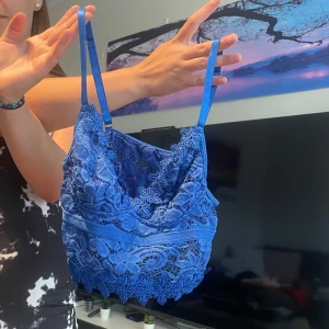 Blå spetsig linnetopp med smala band - Supersnygg blå linnetopp i spets med tunna axelband och blommiga detaljer. Toppen har en croppad passform och vacker spetskant nertill som ger en romantisk vibe. Perfekt att styla till jeans eller kjol för en trendig look.