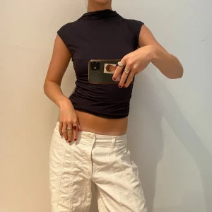 Svart croppad polotopp - Säljer en svart croppad polotopp med tight passform och ärmlös design. Toppen har hög hals och är perfekt för dig som gillar en stilren och edgy look. Passar snyggt till både jeans och kjol.