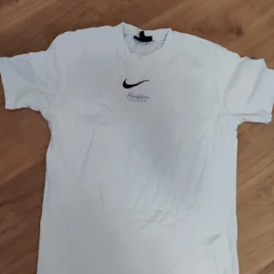 Vit Evolution Season t-shirt med vingar - Vit t-shirt från Evolution Season med svart logga och text framtill. På ryggen finns ett stort, färgstarkt tryck av blå, gröna och gula vingar samt texten 'Evolution Season'. T-shirten har rund hals och korta ärmar, perfekt för dig som gillar unika prints.