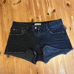 Svarta jeansshorts från Gina Tricot - Snygga svarta Lågmidjade jeansshorts från Gina Tricot. Shortsen har dragkedja och knapp framtill samt bälteshällor. De har lute slitningar på fickorna fram och bak se bild men de ger bara shortsen en cool look. Ett litet håll vid gylfen men inget syns igenom eftersom de är tyg under. Syns knappt (se bild). 200kr eller köp direkt för 150kr utan krångel!