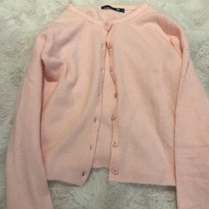 Ljusrosa kofta från 157, XS - Supersöt ljusrosa kofta från 157 i storlek XS. Koftan har rund halsringning, långa ärmar och knäpps med matchande knappar framtill. Mjuk och stickad känsla, perfekt att slänga över en topp för en chill look.