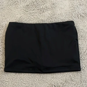 Svart minikjol med shorts - Säljer en svart, tight kortkjol med inbyggda shorts under. Kjolen är enkel och stilren utan mönster, perfekt för dig som gillar en clean look och vill känna dig bekväm när du rör dig. Materialet känns stretchigt och passar bra vid varmt väder.