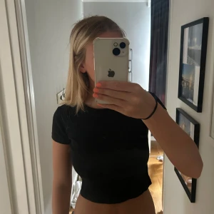 Svart croppad ribbad topp Divided - Svart croppad topp från Divided med ribbad struktur och rund halsringning. Kortärmad och figurnära passform som är enkel att matcha till olika outfits. Perfekt för dig som gillar en clean och stilren look.