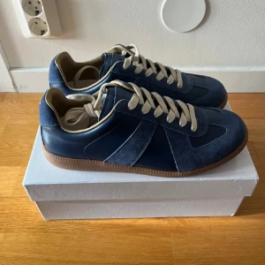 Maison margiela gats - Snygga sneakers från Maison Margiela i mörkblå mocka och skinn med beige snörning och innersida. Klassisk siluett med gummisula och rund tå. Perfekta för dig som gillar stilrena och trendiga skor med premiumkänsla. Obs inte orginal