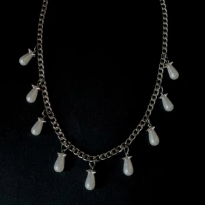 Silverhalsband med droppformade pärlor - Kedjehalsband i silverfärg med nio droppformade vita pärlor som hänger längs hela kedjan. Pärlorna har en snygg glans och ger halsbandet en cool och elegant vibe. Rostfritt stål.