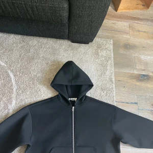 Svart hoodie med dragkedja från Weekday - Svart hoodie från Weekday i storlek S. Tröjan har en klassisk huva, hel dragkedja framtill och stora fickor. Materialet är mjukt och lite tjockare, perfekt för lager-på-lager. Enkel och clean design som funkar till allt.