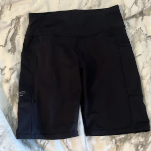 Svarta träningstights-shorts från SOC - Svarta, högmidjade träningstights-shorts från SOC med tight passform. De har bred resår i midjan och praktiska sidfickor. Perfekta för gymmet eller löprundan, tillverkade i stretchigt syntetmaterial som andas. Om funkar också som dom perfekta cykelbyxorna med fickor på sidorna🤍