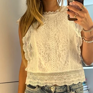 Vit spetsblus  - Superfin vit blus från ONLY Blue Denim i spets med broderade detaljer och vågig kant. Ärmlös modell med hög hals och vackert mönstrad spets över hela toppen. Perfekt att styla med jeans för en fräsch look.
