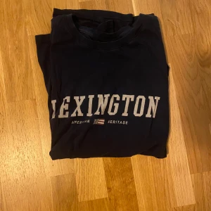 Svart Lexington t-shirt XXL - Svart t-shirt från Lexington i storlek XXL med klassisk vit logga framtill. Skön passform och rund halsringning, perfekt för en chill och stilren look. Tillverkad i mjuk bomull som känns nice mot huden.