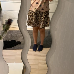 Leopardmönstrad volangkjol 170 - Säljer en kort volangkjol med leopardmönster i beige, brunt och svart. Kjolen har en luftig och flowy passform med resår i midjan för extra komfort. Perfekt för dig som vill sticka ut med en trendig och djärv look.