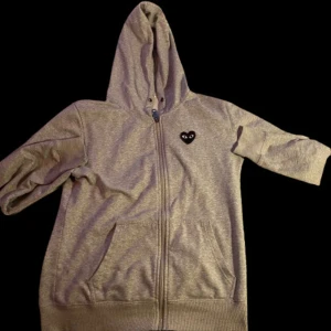 Grå hoodie från Comme des Garçons - Grå hoodie med dragkedja från Comme des Garçons Play. Ikoniskt svart hjärta med ögon på bröstet och stort hjärta på ryggen. Mjuk bomull, huva och fickor framtill. Perfekt för dig som gillar streetstyle och vill sticka ut. Priset går att diskutera!! MVH