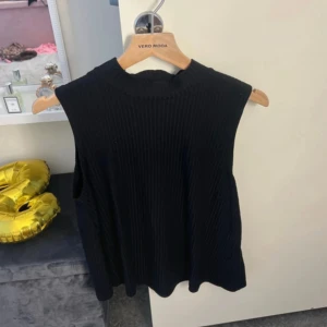 Svart ribbad ärmlös topp  - Svart ärmlös topp från Pieces med ribbad struktur och hög hals. Perfekt att styla med jeans eller kjol för en clean look. Tidlös och enkel design som passar till många outfits.