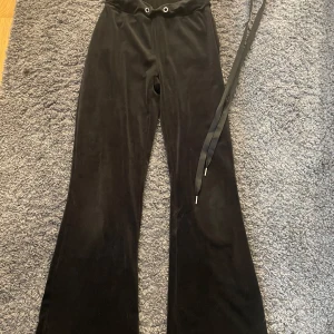 Svarta mjukisbyxor från Gina Tricot - Svarta mjukisbyxor från Gina Tricot i supermjuk velour med hög midja och vida ben. Byxorna har snörning i midjan och stora bakfickor för en chill och trendig look. Perfekta för dig som gillar bekvämt men ändå vill se snygg ut.