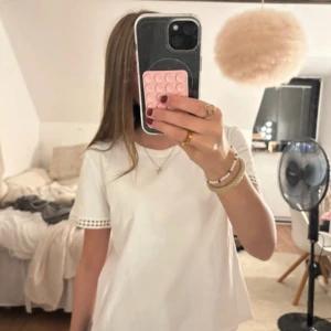 Vit t-shirt med spetsdetalj - Vit t-shirt i bomull med korta ärmar och snygg spetsdetalj längst ut på ärmsluten. Enkel och fräsch modell med rund halsringning, lånade bilder!