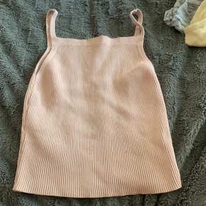 Ljusrosa ribbad linnetopp från Dilvin - Supersöt ljusrosa ribbad linnetopp från Dilvin. Toppen har raka axelband och är figurnära med en enkel, stilren design. Perfekt att matcha med jeans eller kjol för en fräsch look.