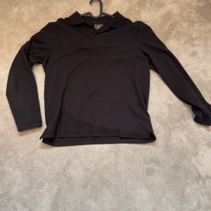 Svart långärmad pikétröja H&M - Svart långärmad pikétröja från H&M med klassisk krage och knäppning framtill. Tröjan är ribbad och har en stilren, enkel look som passar perfekt till jeans eller chinos. Tillverkad i mjuk bomull för en bekväm känsla hela dagen. Använd 1 gång 