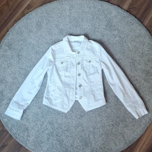 Vit jeansjacka från 2-Biz, stl S - Fräsch vit jeansjacka från 2-Biz i storlek S. Klassisk modell med silverfärgade knappar framtill och på ärmslut, två bröstfickor och figurnära passform. Jackan är använd 1 gång och har extra knappar som följer med. Den harfått en liten smink fläck som knappt syns, därav priset! Original pris 800kr