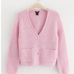 Rosa ribbad kofta - Superfin ljusrosa kofta från Monki med ribbad stickning, v-ringning och knappar framtill. Tröjan har två stora fickor och långa ärmar. Perfekt att slänga över en t-shirt för en chill look.