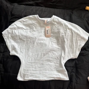 Vit vid topp från Nelly - Säljer den populära toppen från Nelly då den inte har kommit till användning. Den sitter tajtare runt midjan och pösigare vid ärmarna. Prislappen sitter kvar.  Nypris 249kr