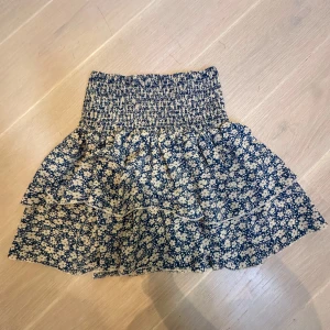 Blommig volangkjol med blommönster  - Supersöt kort kjol med blått och vitt blommönster och volanger. Oanvänd!