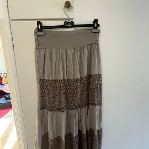 Militärgrön långkjol med spetsdetaljer - Säljer en militärgrön långkjol som har snygga spetsdetaljer i mönstrade partier. Materialet känns lätt och flowy. Säljer då den tyvärr är för kort för mig och endast använd två ggr.