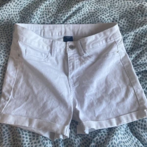 Vita jeansshorts från Vero Moda - Snygga vita jeansshorts från Vero Moda med klassisk femficksdesign och uppvikta benslut. Perfekta för varma dagar och enkla att matcha med allt. Stängs med knapp och dragkedja framtill. Stilrena och fräscha shorts för sommaren.