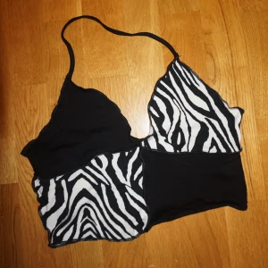 Zebramönstrad croppad linne-topp - Säljer en croppad linne-topp med svart och zebramönstrad patchwork-design och bak rygg. Toppen har smala axelband och är perfekt för dig som vill sticka ut med en edgy stil. Mjuk och stretchig känsla, passar till både jeans och kjol.
