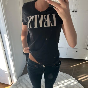 Svart Levi's t-shirt med vit logga - Svart t-shirt från Levi's med klassisk vit logga framtill. Modellen är kortärmad med rund halsringning och normal passform. Tillverkad i mjuk bomull som är skön mot huden. Perfekt till jeans eller shorts för en chill look.