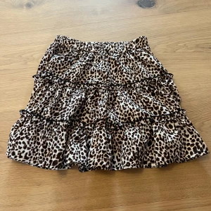 Leopardmönstrad volangkjol - Kort kjol med leopardmönster och flera volanger. Kjolen har resår i midjan och är sydd i ett glansigt, lätt material som ger ett snyggt fall. Perfekt för dig som vill sticka ut med en trendig look. Kjolen har ingen lapp så vet inte vart den är ifrån och skulle gissa att den är i storlek xs