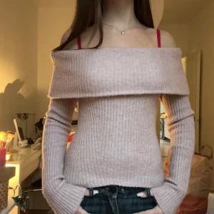 Ljusrosa ribbad offshoulder tröja - Superfin ljusrosa stickad tröja med ribbad struktur och offshoulder-modell. Tröjan har långa ärmar och en bred, nedvikt kant över axlarna som ger en snygg och trendig look. Perfekt att styla med jeans eller kjol för en chill vibe.