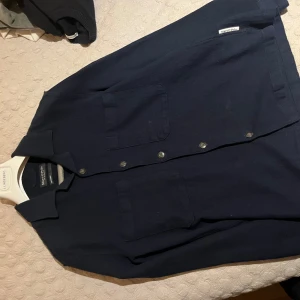 Mörkblå overshirt från Marc O'Polo - Snygg mörkblå overshirt från Marc O'Polo med klassisk krage, två stora bröstfickor och knäppning framtill. Skjortan är tillverkad i ett mjukt bomullstyg och har en stilren, minimalistisk look som passar perfekt till lager-på-lager.